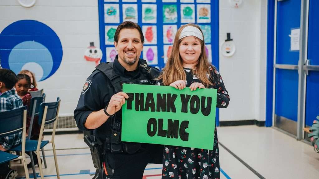 Police officer and community member holding a 'Thank You OLMC' sign during Baby Jesus Lunch