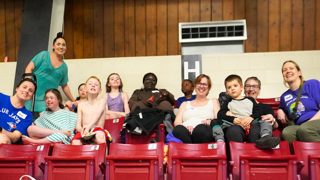 Students, parents and instructors sitting at the pool arena at the Annual Swim Meet